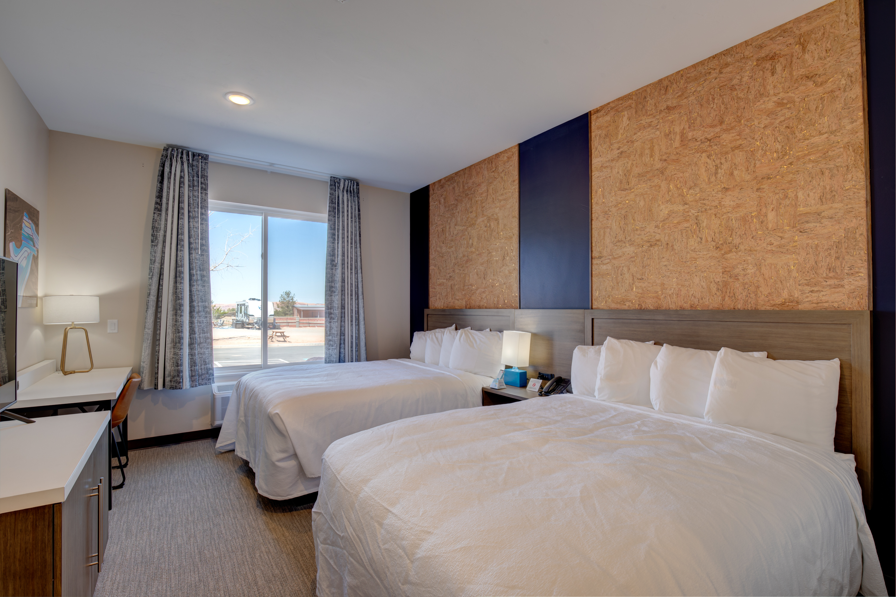 A hotel room with two queen beds, a desk, and a window