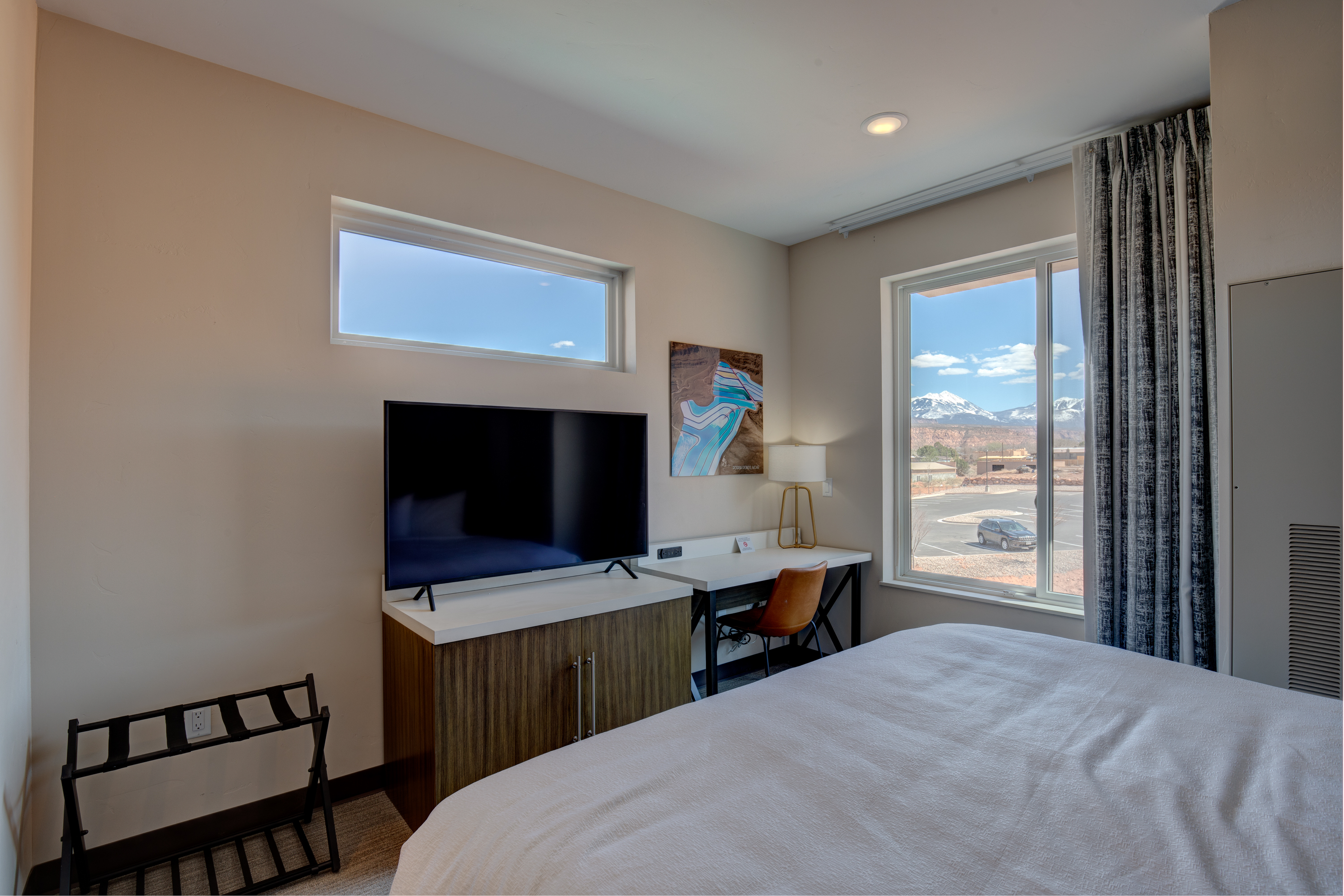 A hotel room with a bed, desk, TV, and window showing a mountain view.