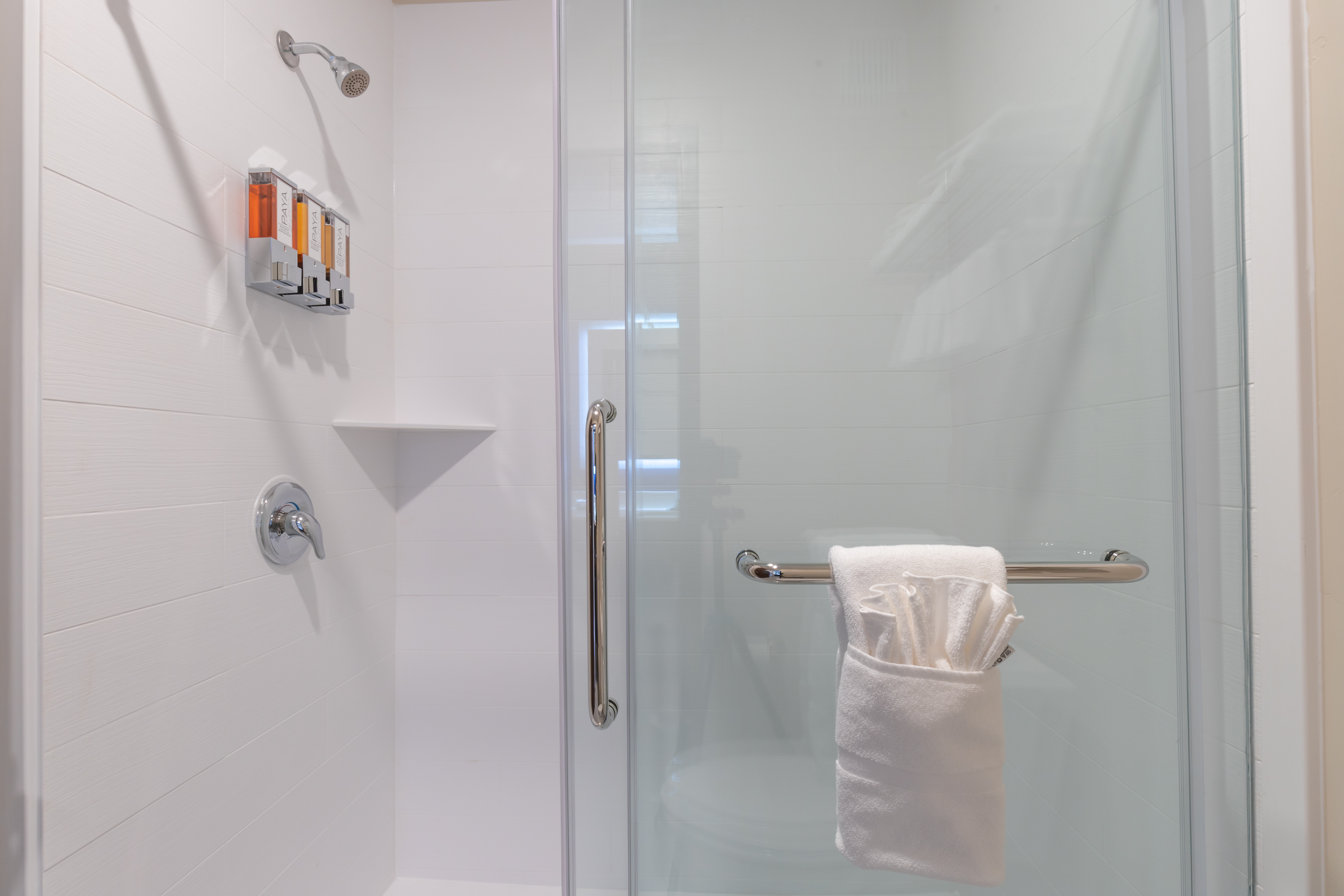 A clean and modern bathroom shower with a glass door, shower caddy, and towels.